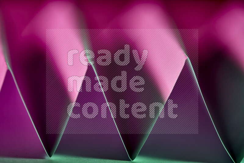 A close-up abstract image showing sharp geometric paper folds in green and purple gradients