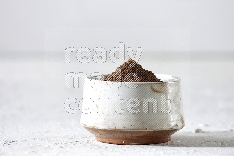 A beige ceramic bowl full of cloves powder on a white flooring