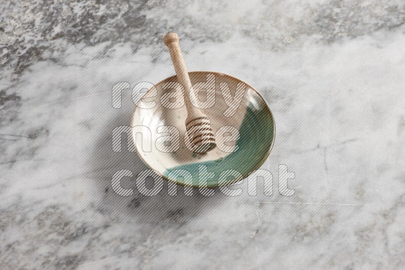 Multicolored pottery plate with wooden honey dipper in it on grey marble background