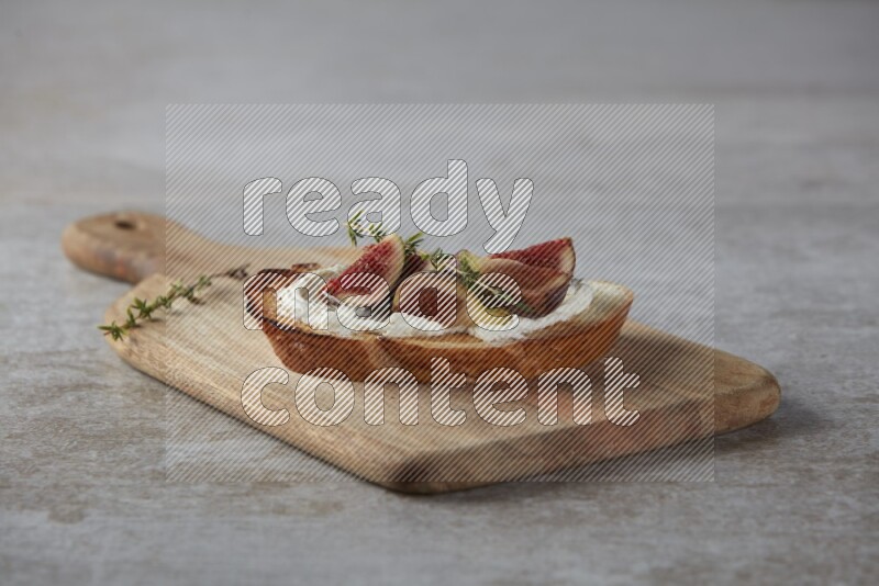 quarters of figs with cream cheese on toasted sourdough slice on a wooden board on textured grey background