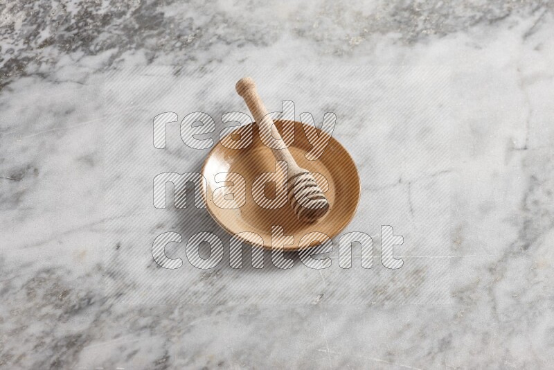 Beige pottery plate with wooden honey dipper in it on grey marble background