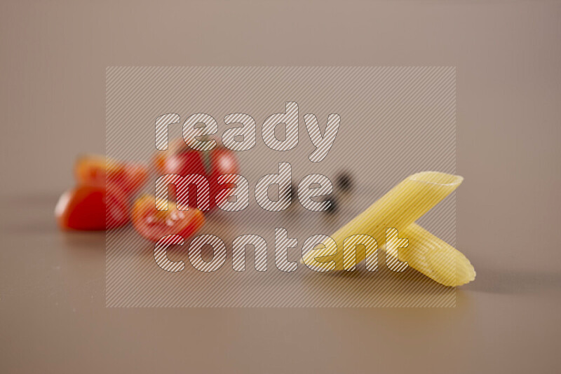 Raw pasta with different ingredients such as cherry tomatoes, garlic, onions, red chilis, black pepper, white pepper, bay laurel leaves, rosemary and cardamom on beige background