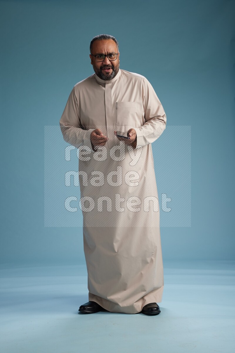 Saudi Man without shimag Standing texting on phone on blue background