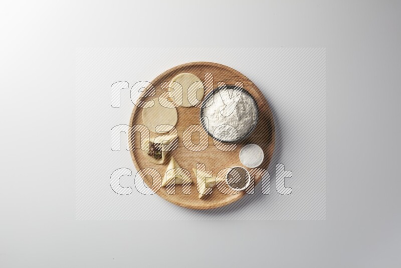 two closed sambosas and one open sambosa filled with meat while flour, salt, and black pepper aside in a wooden dish on a white background
