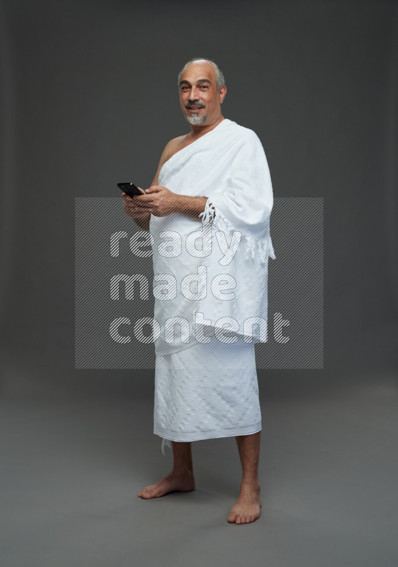 A man wearing Ehram Standing texting on phone on gray background