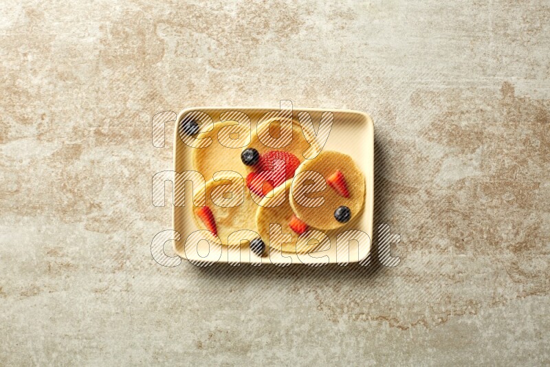 Five stacked mixed berries mini pancakes in a rectangular plate on beige background