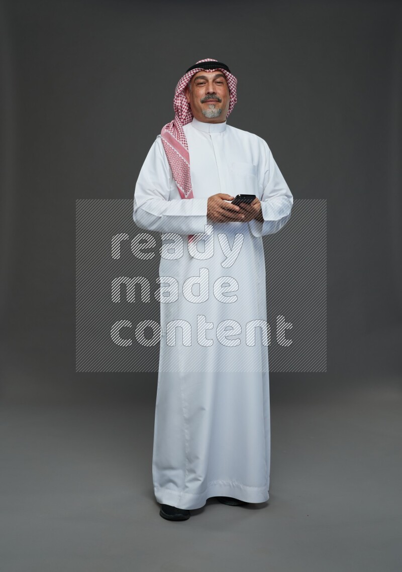 Saudi man with shomag Standing texting on phone on gray background