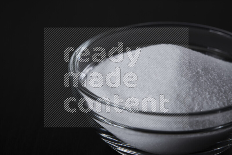 A glass bowl full of fine table salt on black background