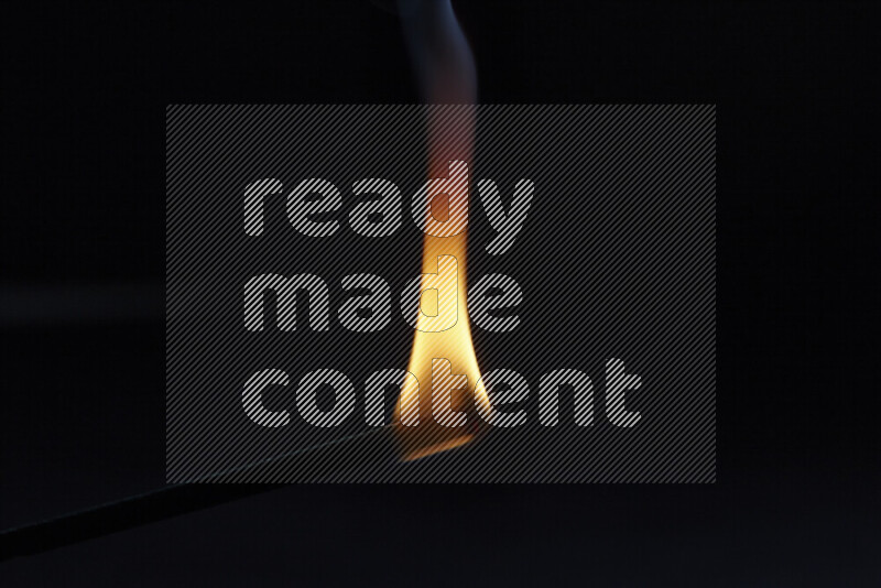 A burning incense stick isolated on dark backdrop