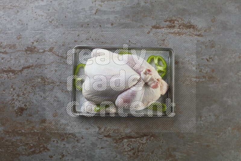 whole Raw chicken on a small oven trey direct on a rustic grey background