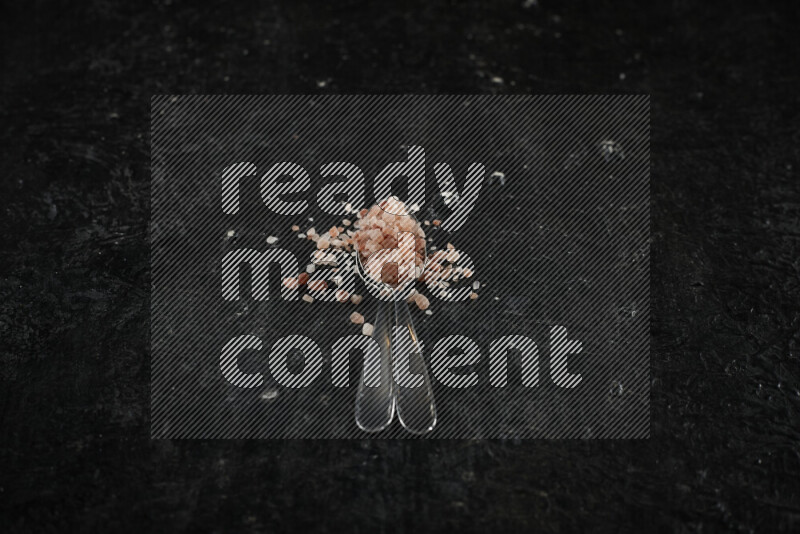 ملعقتان معدنيتان ممتلئتان بملح الهيمالايا الوردي على خلفية سوداء