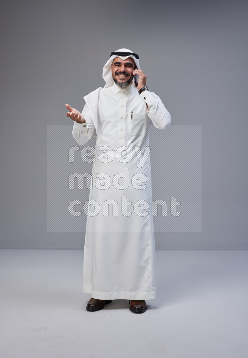 Saudi man Wearing Thob and white Shomag standing talking on phone on Gray background