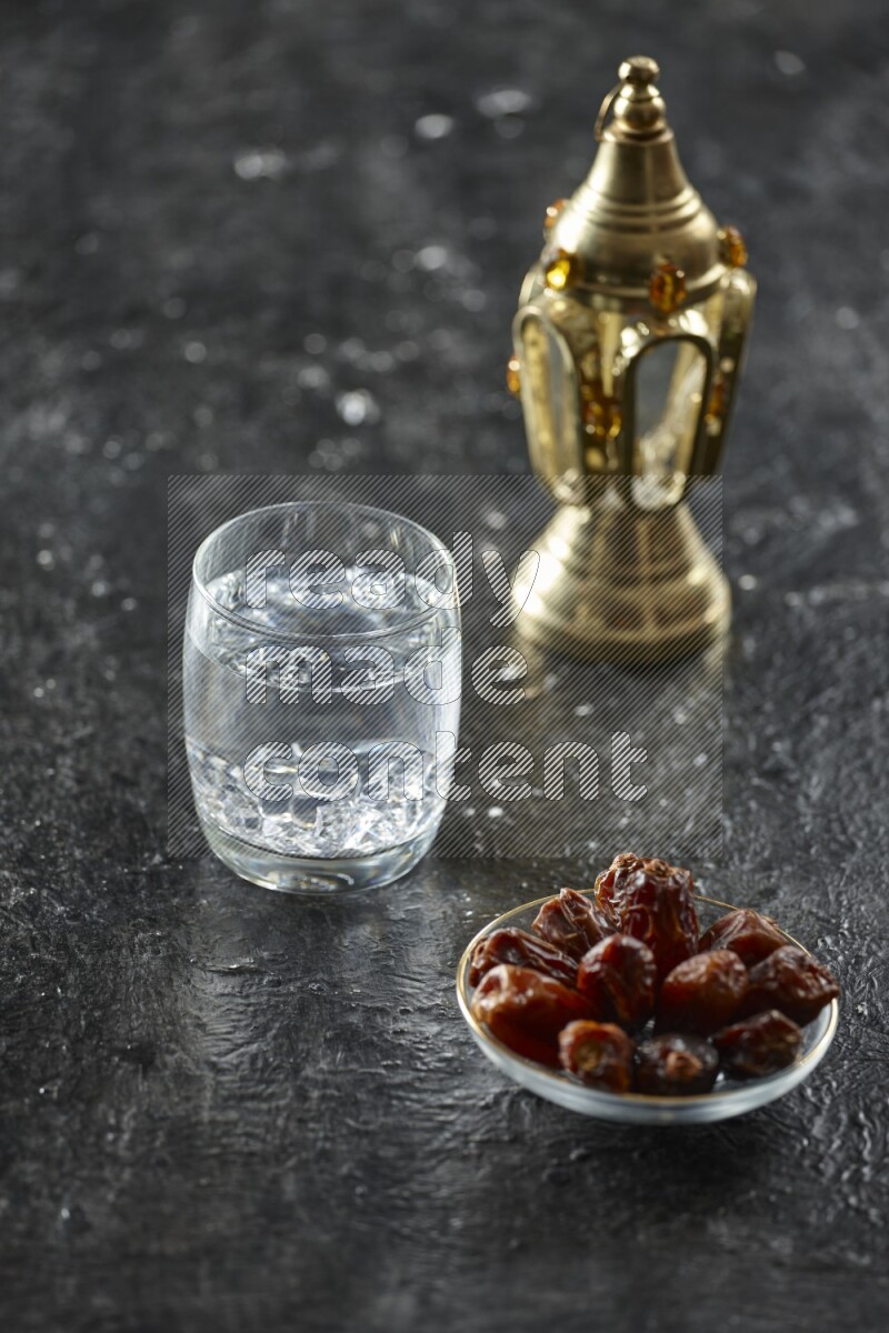 A golden lantern with different drinks, dates, nuts, prayer beads and quran on textured black background