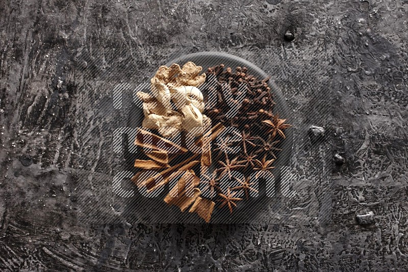 Ginger, cloves, star anise and cinnamon sticks on a black plate on textured black background