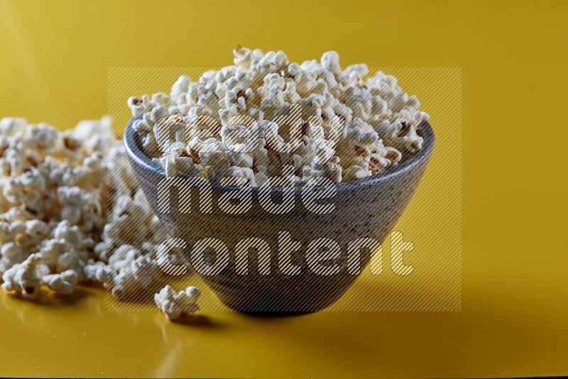 A multicolored pottery bowl full of popcorn with popcorn beside it on a yellow background in different angles