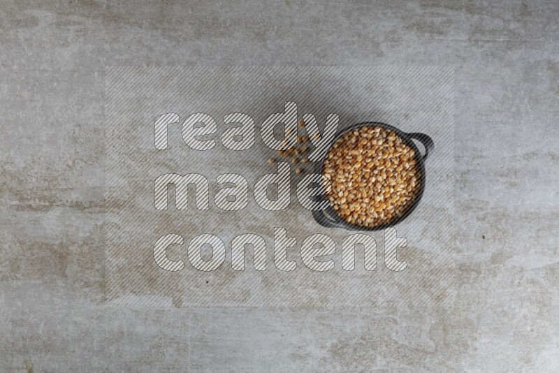 corn kernel in a black handheld ceramic bowl on a grey textured countertop
