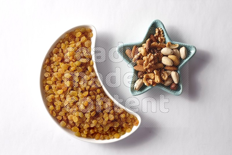 Raisins in a crescent pottery plate and a star shaped plate with mixed nuts on white background