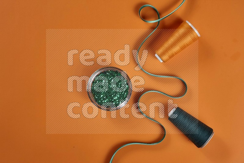 Green sewing supplies on orange background