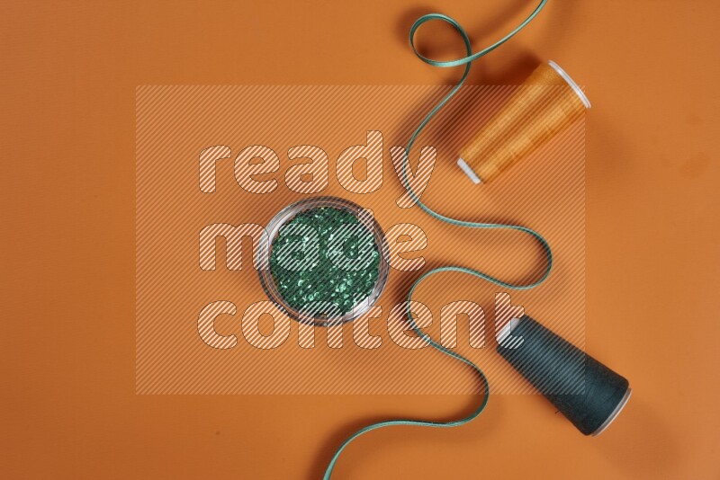A green and orange collection of sewing and tailoring tools arranged on a orange background