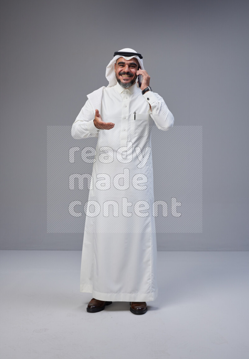 Saudi man Wearing Thob and white Shomag standing talking on phone on Gray background