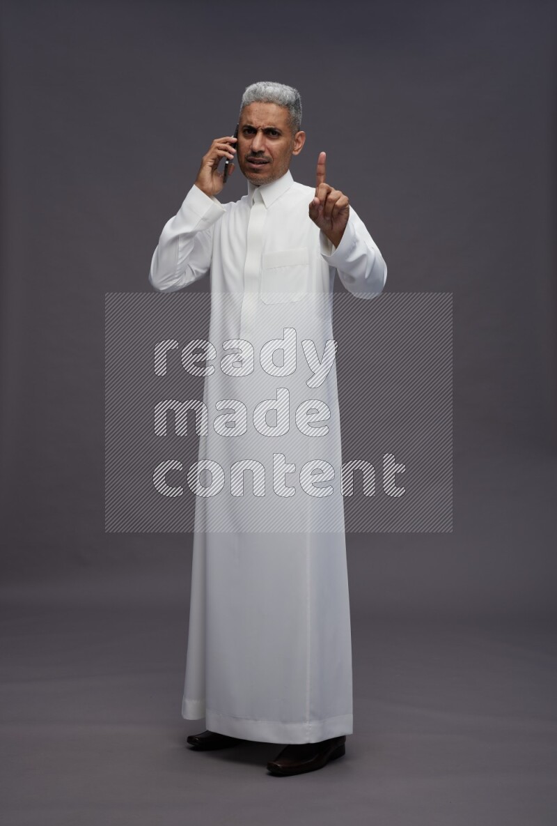 Saudi man wearing thob standing talking on phone on gray background