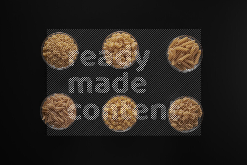 Different pasta types in 6 glass bowls on black background