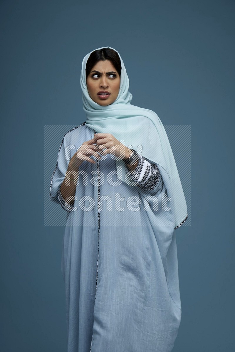 A woman posing in a blue background wearing a blue Abaya with hijab