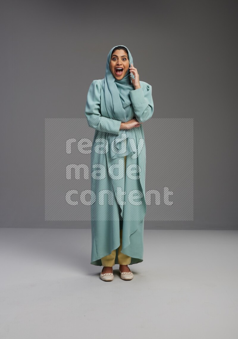 Saudi Woman wearing Abaya standing talking on phone on Gray background