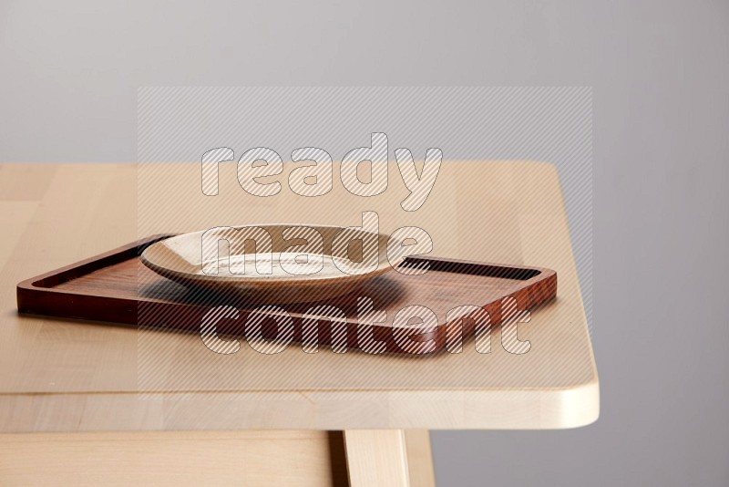 multi-colored pottery Plate placed on a rectangular wooden tray on the edge of wooden table