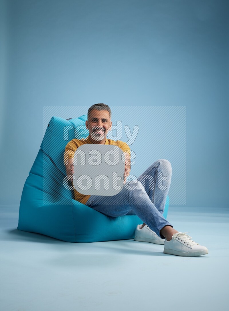 A man sitting on a blue beanbag and holding social media sign