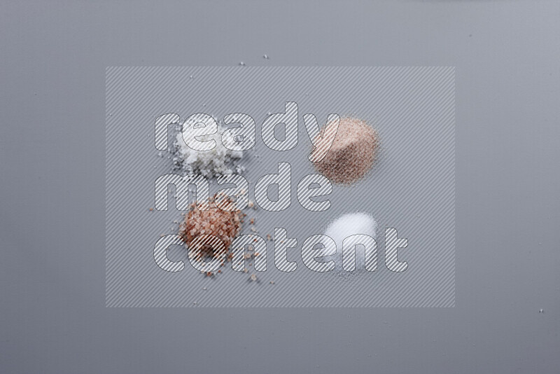 Bunches of table salt, coarse sea salt, fine himalayan salt and coarse himalayan salt on grey background