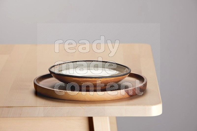 multi-colored pottery Plate placed on a light colored wooden tray on the edge of wooden table