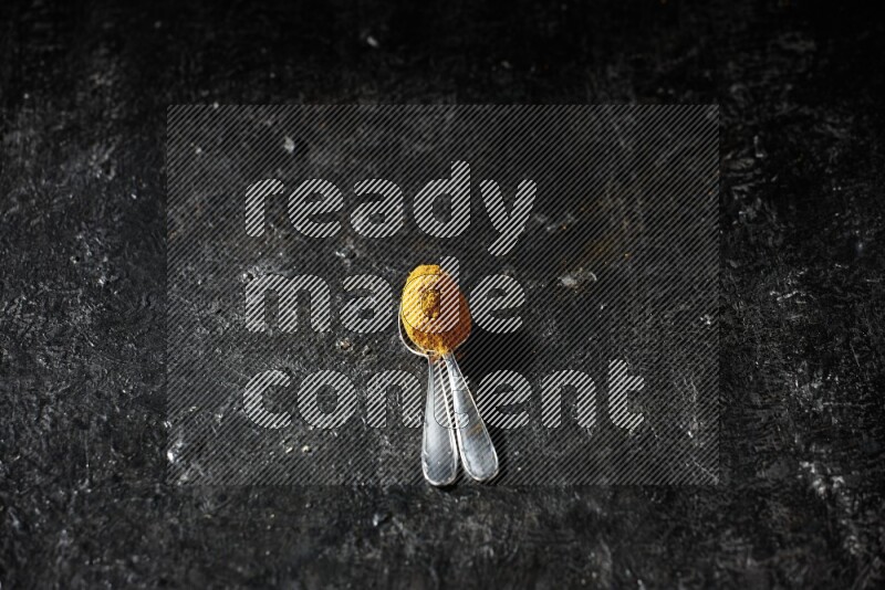 ملعقتان معدنيتان ممتلئتان ببودرة الكركم على خلفية سوداء