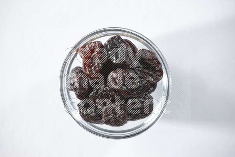 A glass bowl full of dried plums on a white background in different angles
