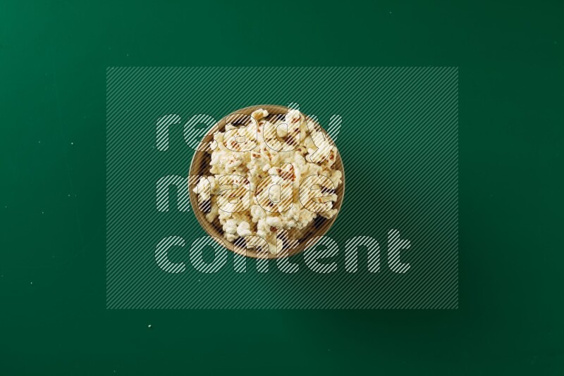 An off white ceramic bowl full of popcorn on a green background in a top view shot