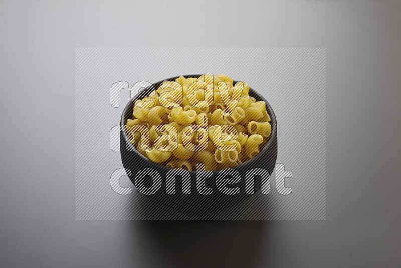 Elbow pasta in a pottery bowl on grey background
