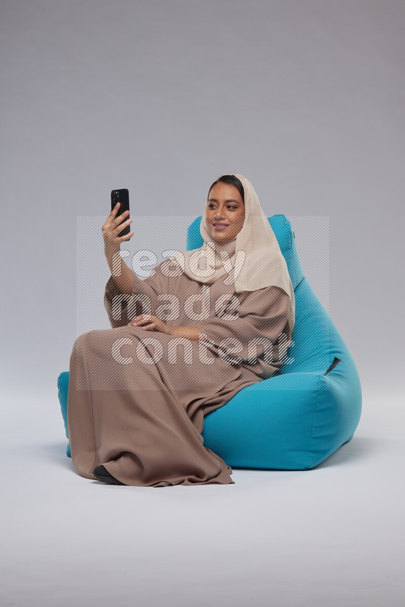 A Saudi woman sitting on a blue beanbag and taking selfie