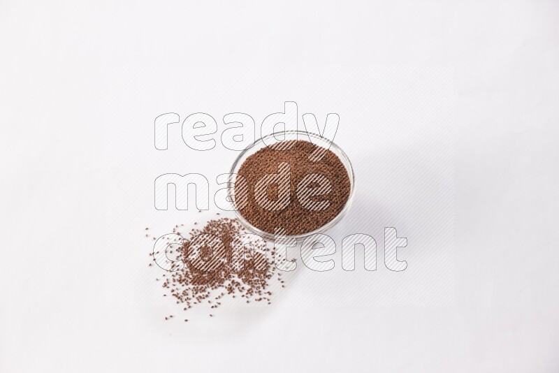 وعاء زجاجي ممتلئ ببذور حب الرشاد مع بعض البذور متناثرة على خلفية بيضاء