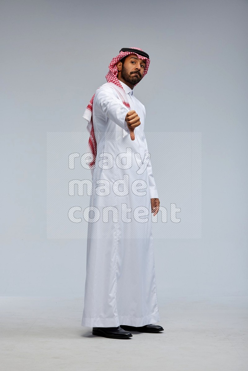 Saudi man Wearing Thob and shomag standing interacting with the camera on Gray background