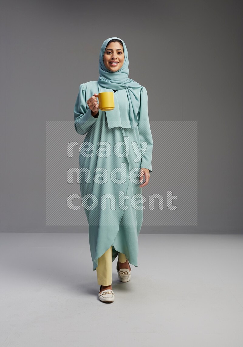 Saudi Woman wearing Abaya standing  holding a mug on Gray background