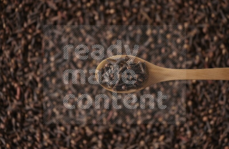 A wooden spoon full of cloves on cloves background and black flooring