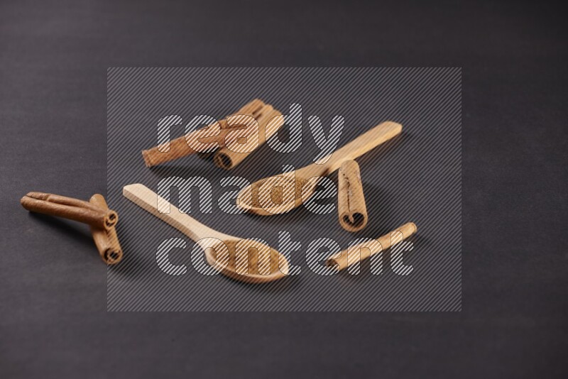 ملعقتان خشبيتان ممتلئتان ببودرة القرفة مع أعواد القرفة على خلفية سوداء