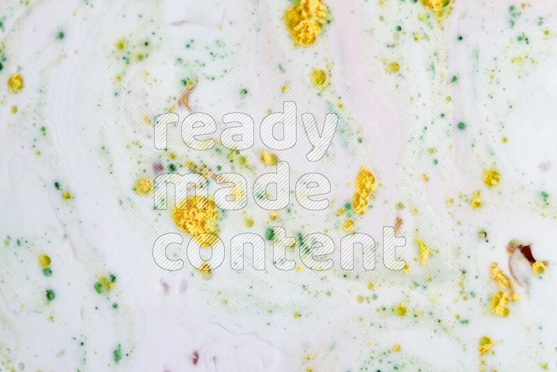 The image captures a splatter of yellow, red and green paint over a white backdrop