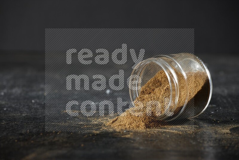 وعاء زجاجي مقلوب ممتلئ ببودرة الكمون والبودرة تناثرت منه على خلفية سوداء