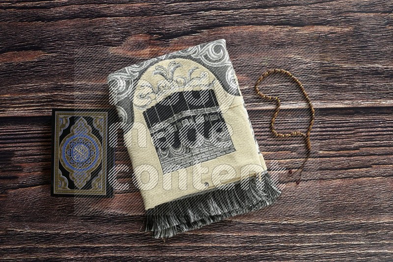 A prayer rug with different elements such as quran and prayer beads on brown wooden background