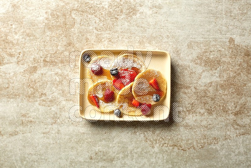 Five stacked mixed berries mini pancakes in a rectangular plate on beige background