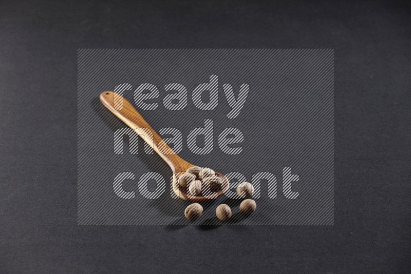 A wooden ladle full of whole nutmeg seeds on a black flooring