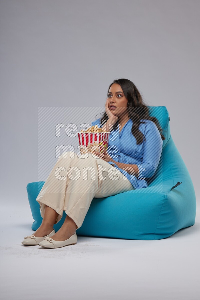 A woman sitting on a blue beanbag and eating popcorn
