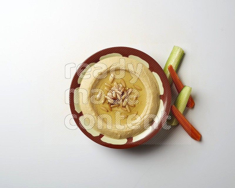 Hummus in a traditional plate garnished with pine nuts on a white background