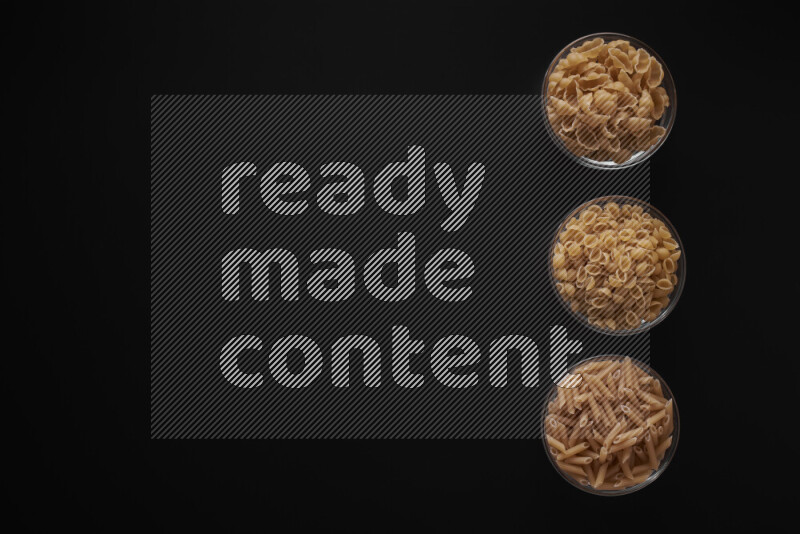 Different pasta types in 3 glass bowls on black background